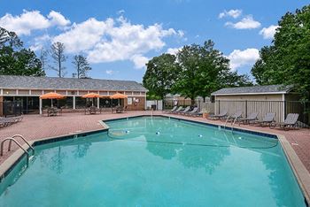 A swimming pool with lounge chairs and umbrellas in front of a building